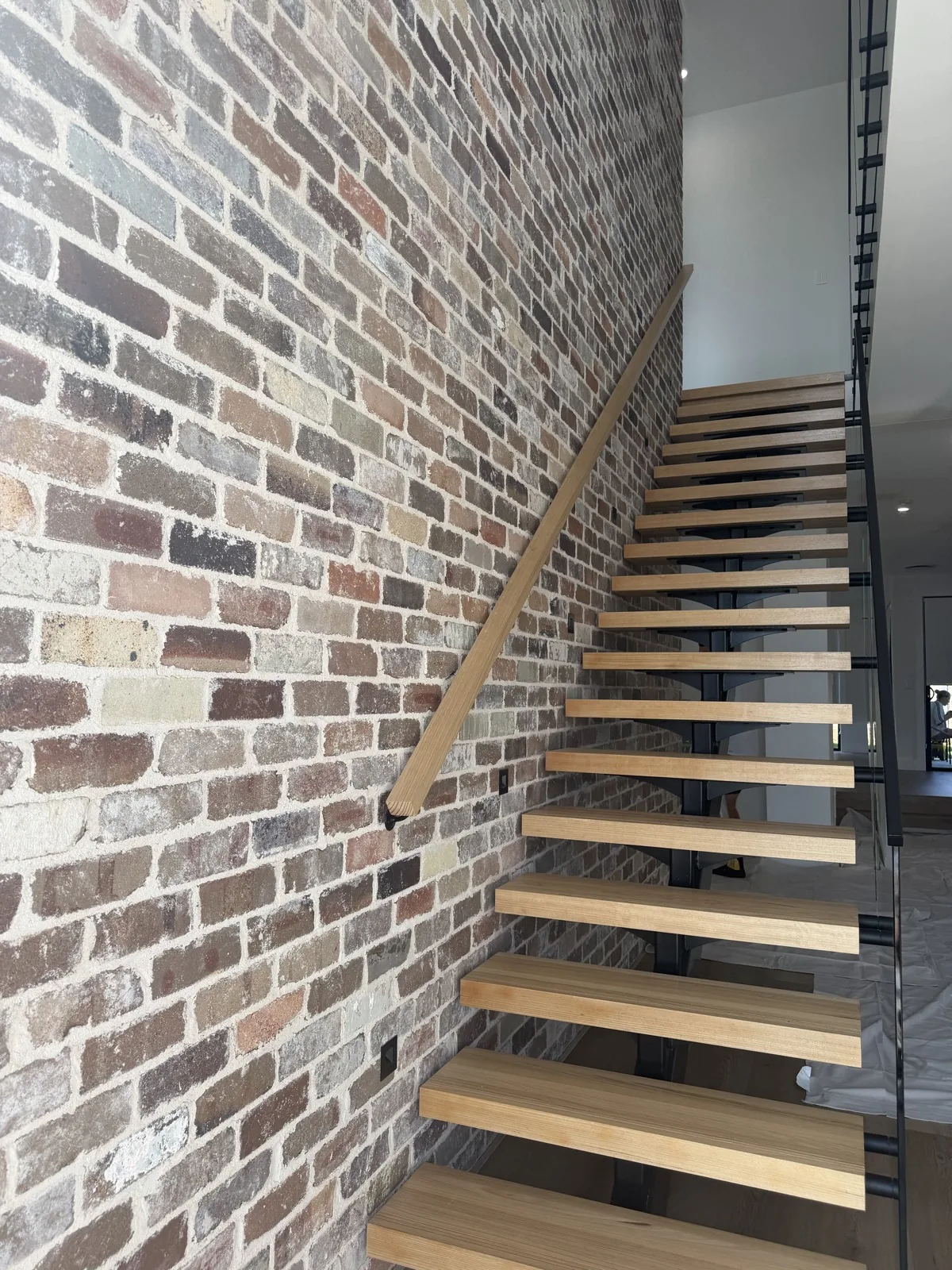 Floating timber staircase beside a feature brick wall, with painted white walls