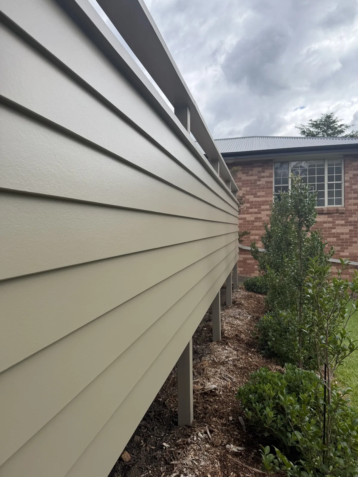 Close view along sage green weatherboard cladding beside a garden